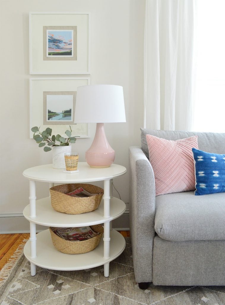 round white three tiered bamboo side table with pink lamp and gray sofa