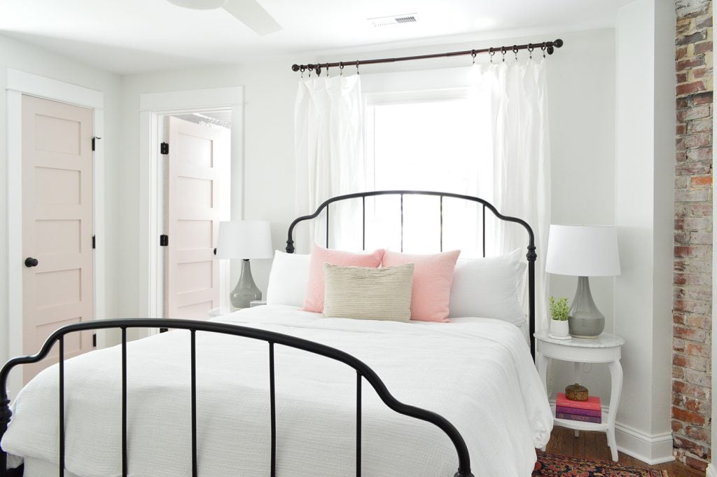 Main Bedroom In Historic Duplex Beach House With Exposed Brick Fireplace | Iron Bedframe | Pink White Truffle Doors