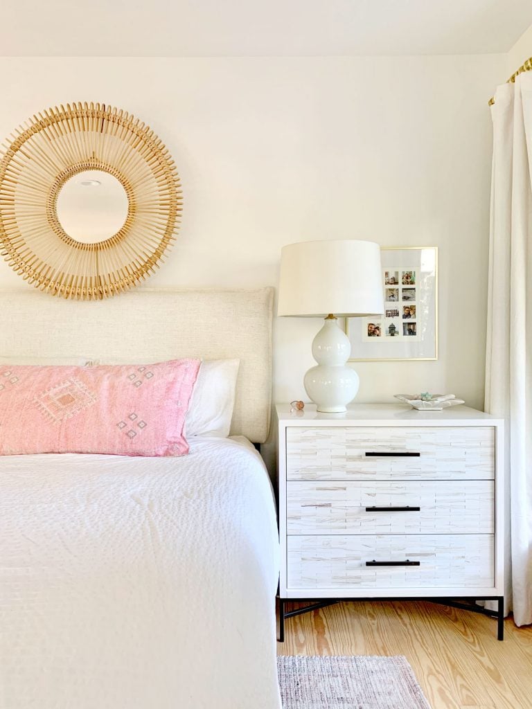Linen headboard on bed with white bedding and inlay dresser as nightstand
