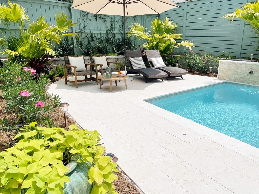 Backyard pool with sitting area under umbrella surrounded by tropical plants
